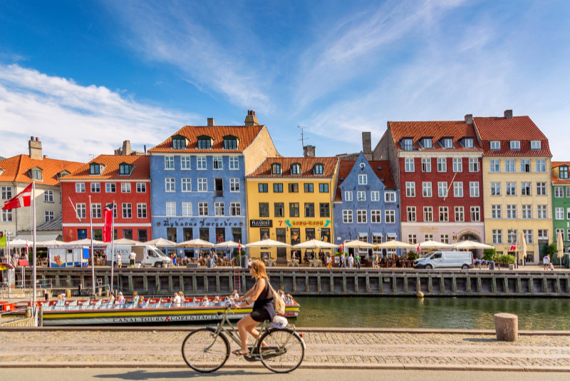 Copenhagen iconic view. Famous old Nyhavn port with colorful medieval houses, tourist ship and woman on a bicycle in the center of Copenhagen. Selective focus